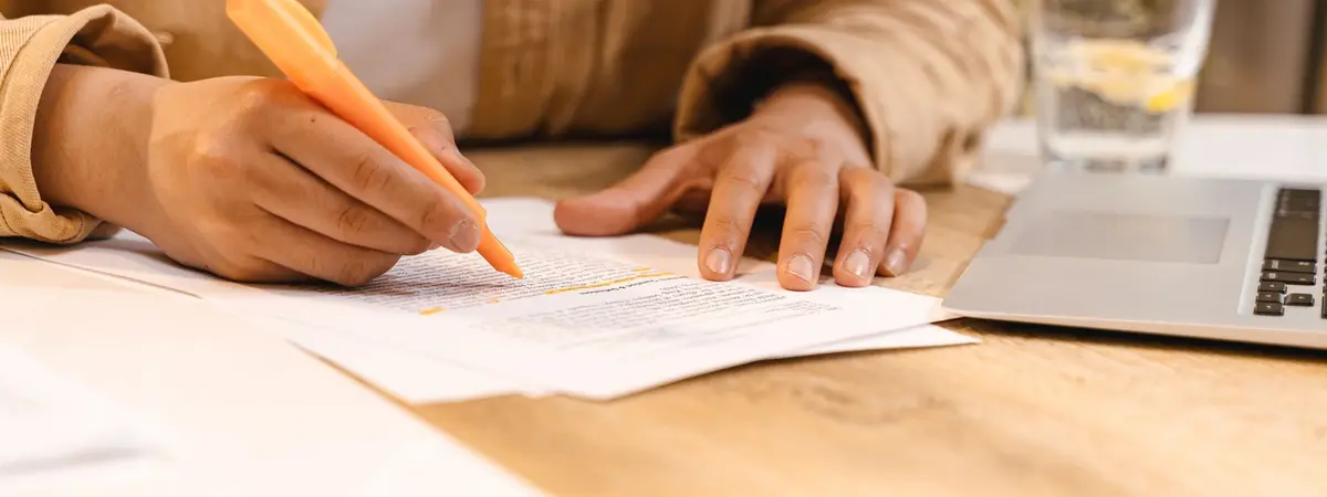 A person highlighting notes at a desk beside a laptop