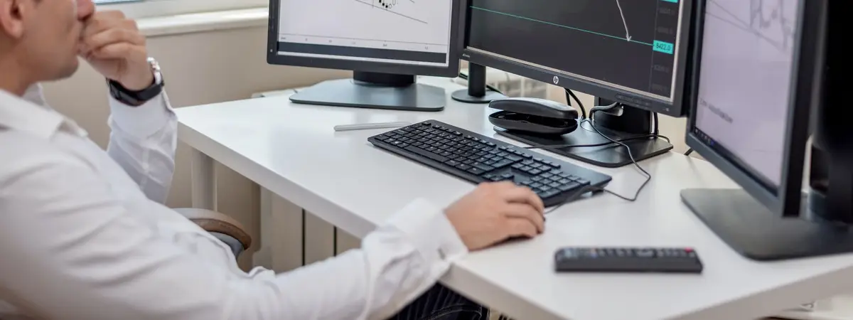 An analyst at a desk working across several monitors of financial data
