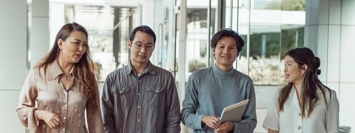 Four colleagues talking together in an office corridor, one holding a laptop