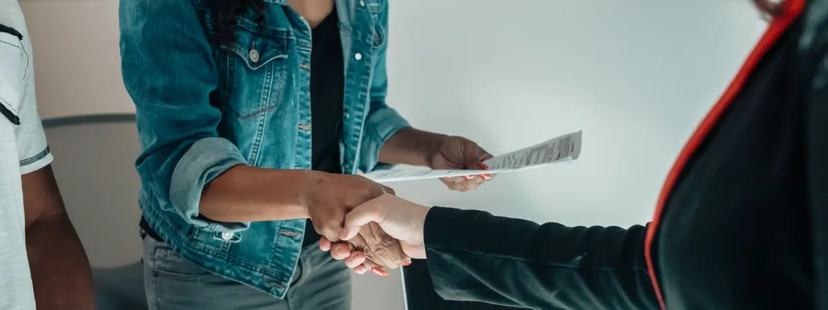Two people shaking hands across a desk after an interview