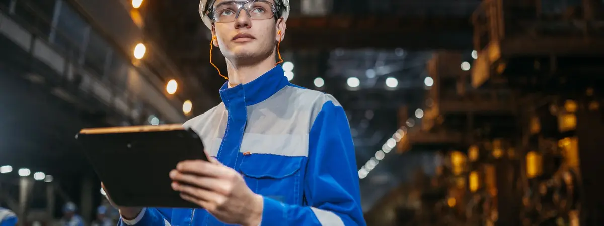 A manager in safety gear checking a tablet on a factory floor