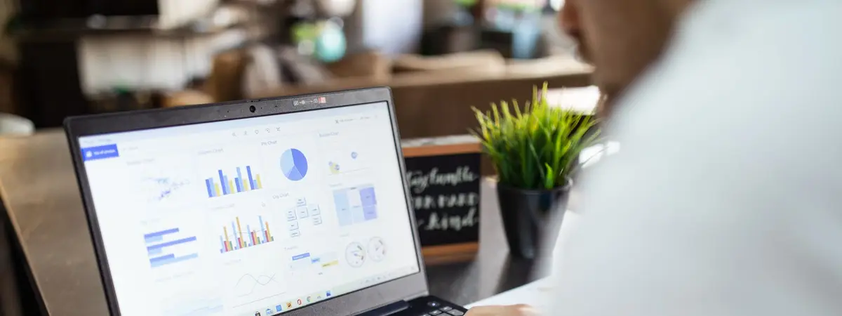 A laptop showing charts and graphs beside printed reports